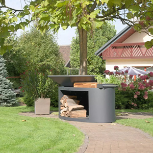 Barbecue design en acier intégré dans un jardin aménagé avec pelouse et plantations